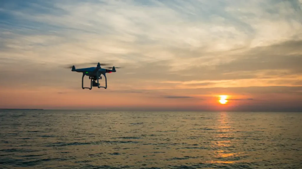 A quadcopter flying over the sea at sunset