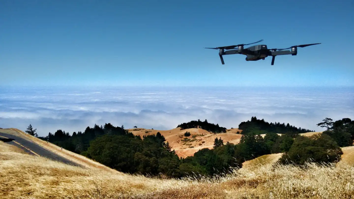 A drone flying over green hills under a cloudy sky